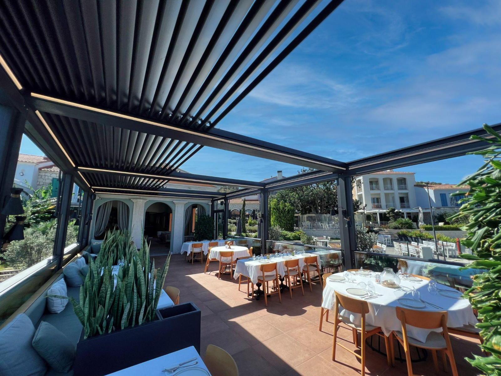 A restaurant featuring an outdoor dining area covered by a stylish pergola, providing shade and ambiance for guests.
