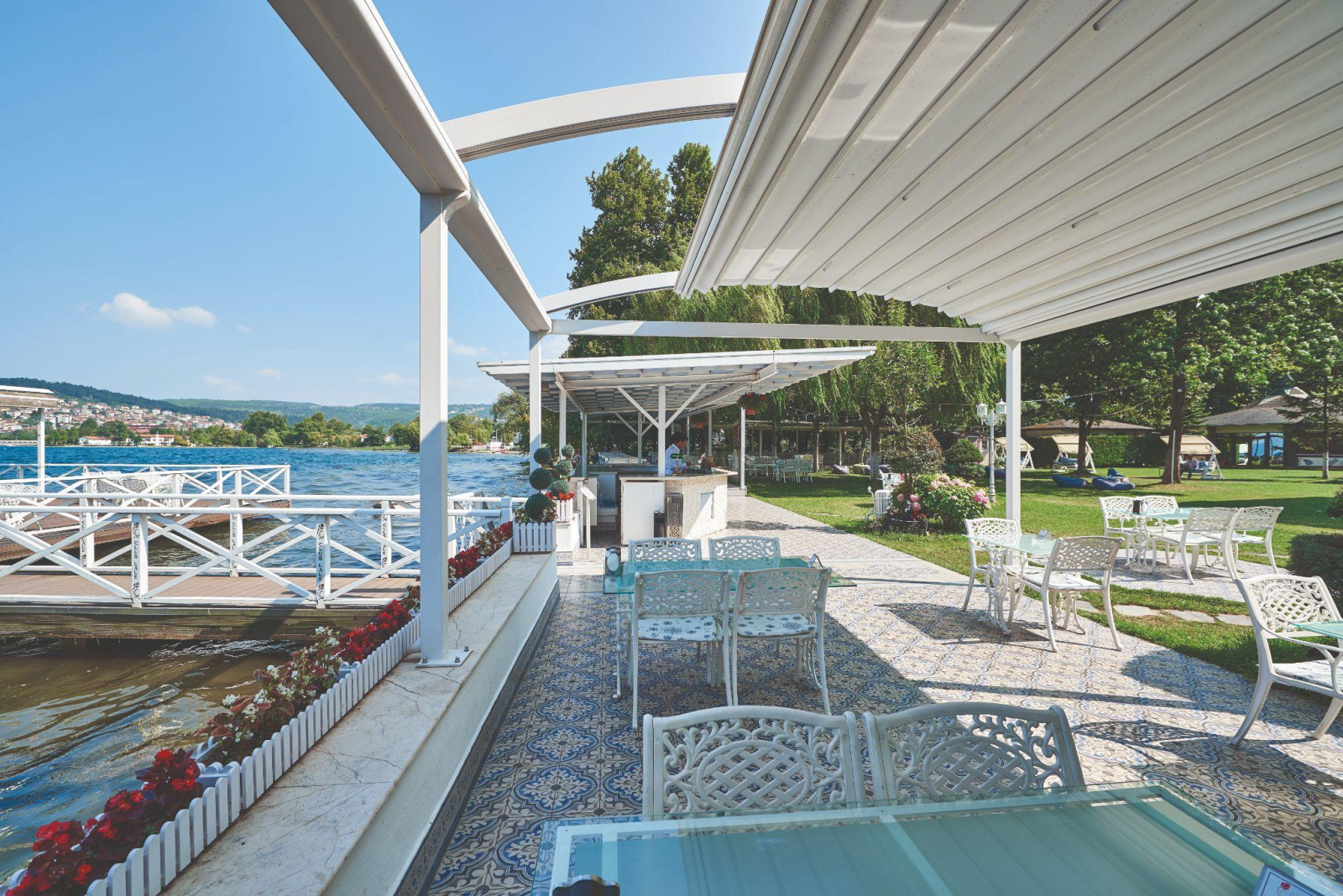 Outdoor restaurant on the waterfront featuring tables and chairs under a pergola, inviting a relaxed dining atmosphere.