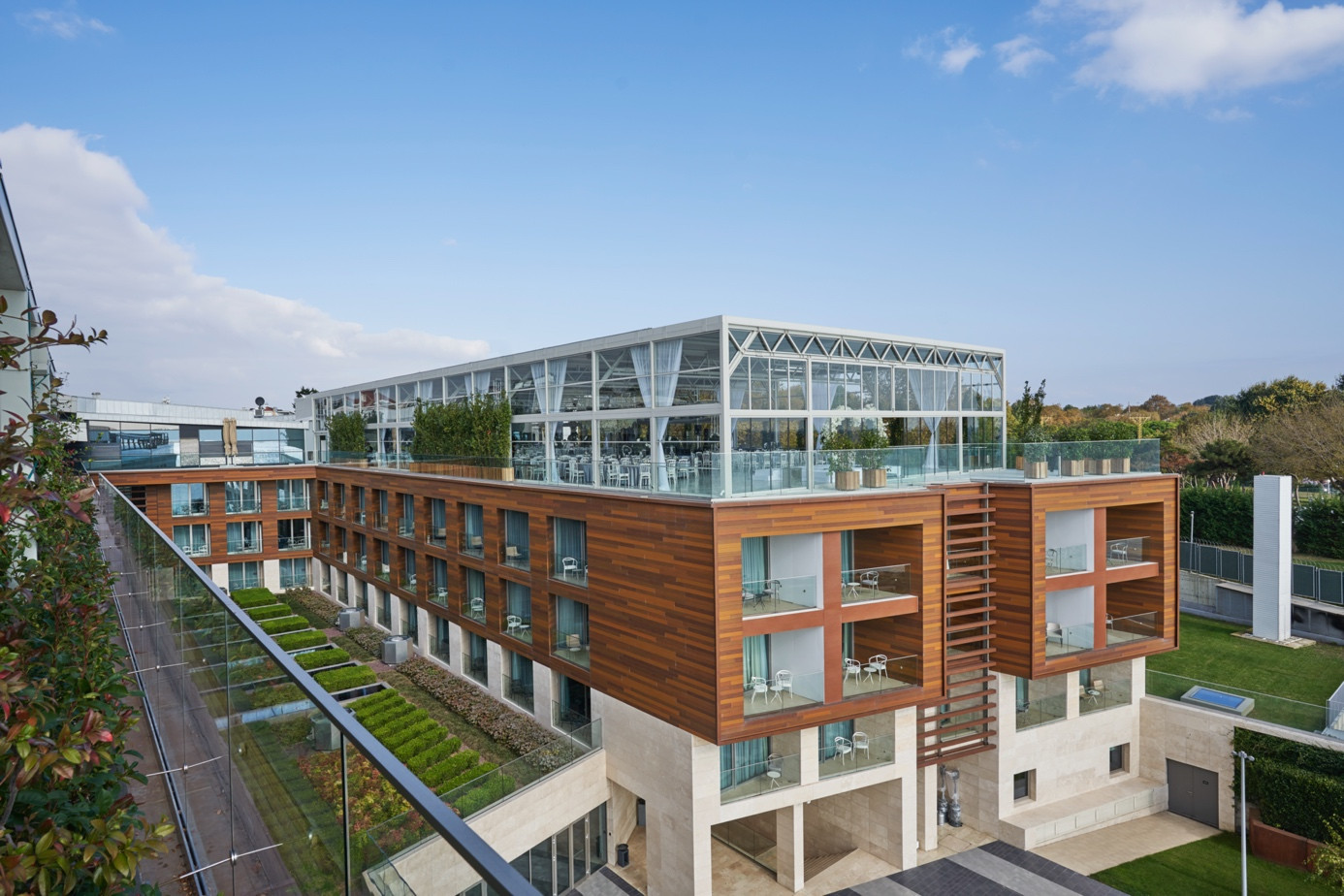 The modern building with glass and wooden balconies draws attention with its pergola systems that are compatible with the space.